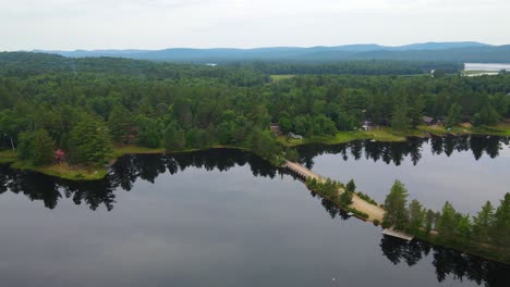 drone shot of pine trees reflecting across the still waters of a lake in the mountains of upstate new york