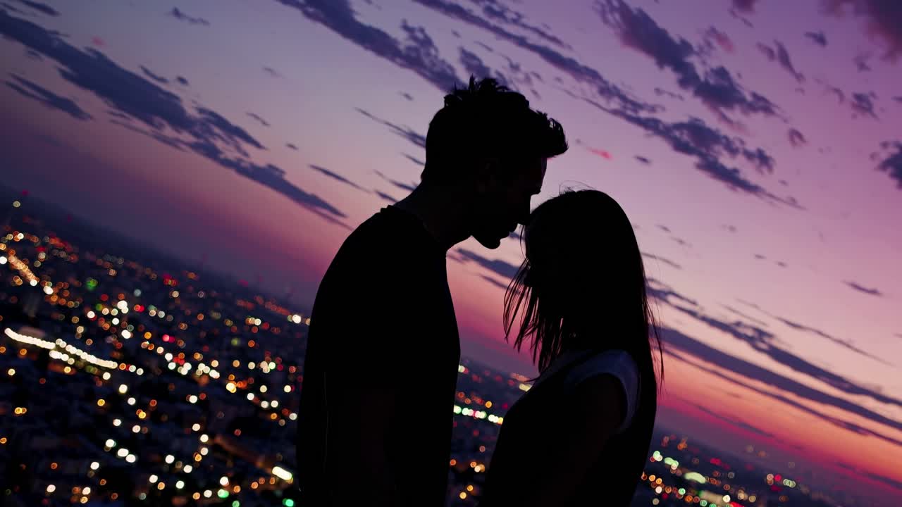 Silhouetted couple in a romantic embrace at sunset, city lights twinkling below