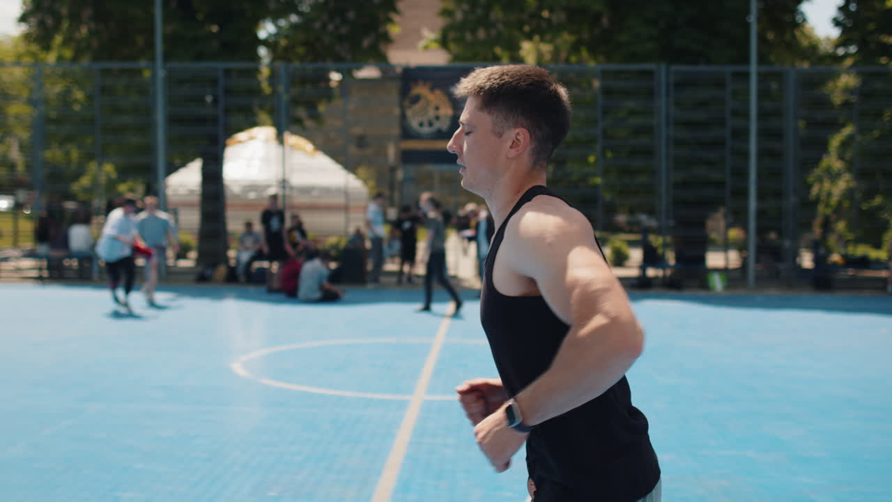 Athletic caucasian sports man in sportswear jogging running on urban basketball court outdoors