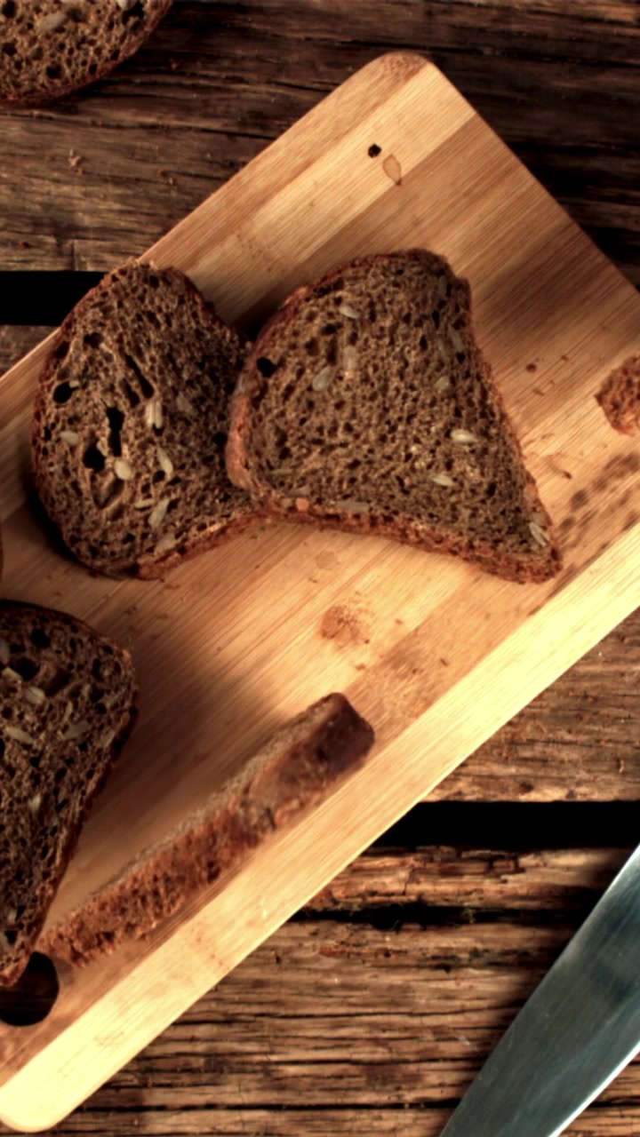 Slices of Dark Rye Bread with Seeds Falling onto a Wooden Board