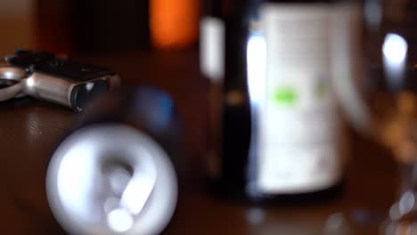 Handgun-lying-on-coffee-table-with-blurred-empty-alcohol-containers-in-foreground-and-burning-woodstove-in-background--Slider-from-right-to-left