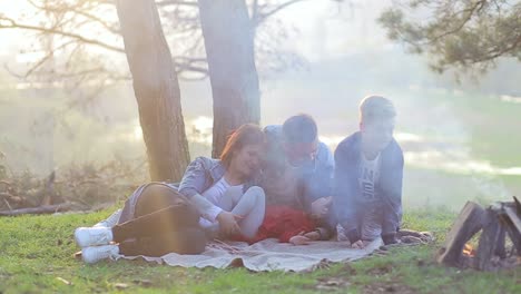 family on vacation for a picnic with a fire camping travel tourism hike and people concept happy family sitting on bench and drinking hot tea from cups at camp fire in woods
