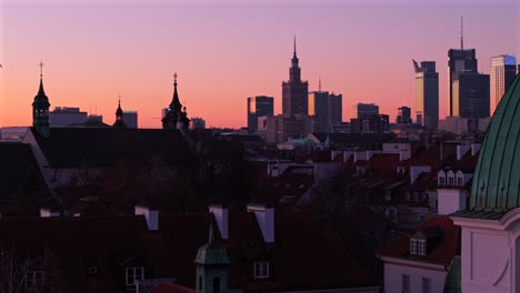 drone pullback backward over warsaw skyline at sunrise, featuring st casimir church, palace of culture, and varso tower, building silhouettes with glow of light