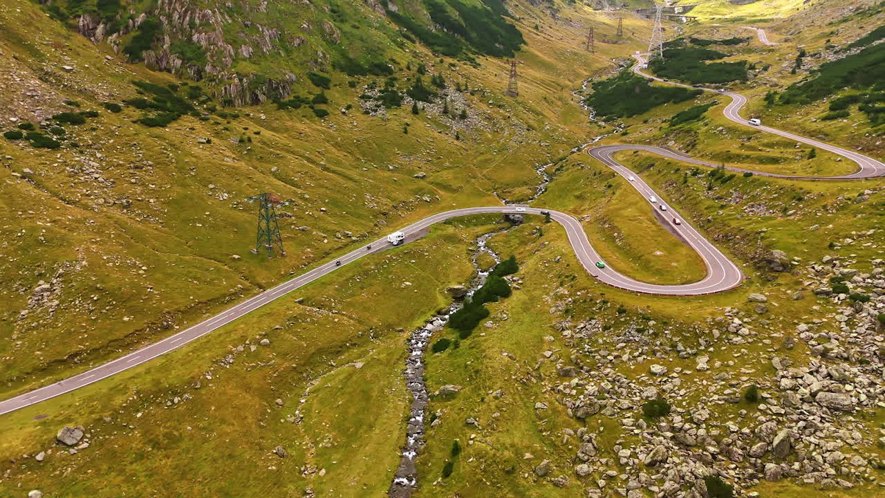 Following cars riding by the wavy road. Drone footage along Transfagarash highway in the Carpathian Mountains, Romania