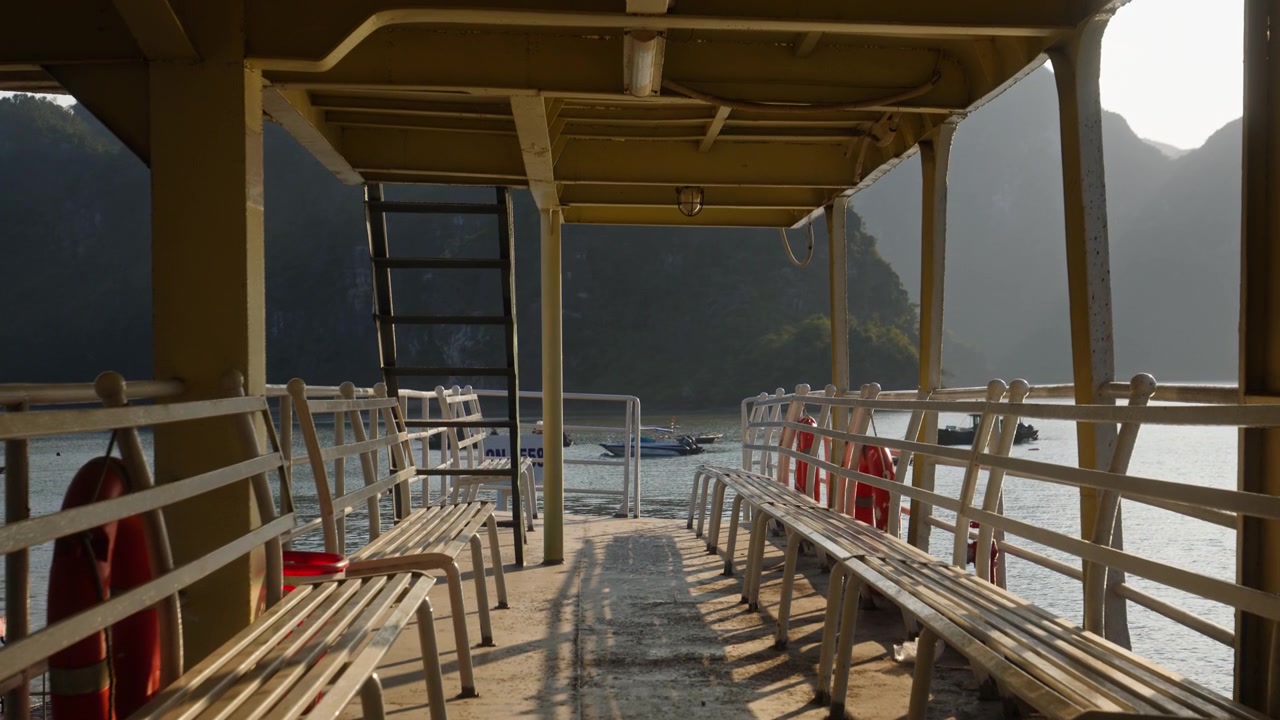 Blick vom schattigen Holzpassagierdeck eines rustikalen Ausflugsbootes, das an massiven Kalkstein-Karstbergen und Klippen in der Ha Long Bucht vorbeifährt. Weitwinkelaufnahme.