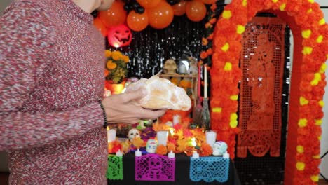 putting bread as offering on decorated mexican day of the dead altar