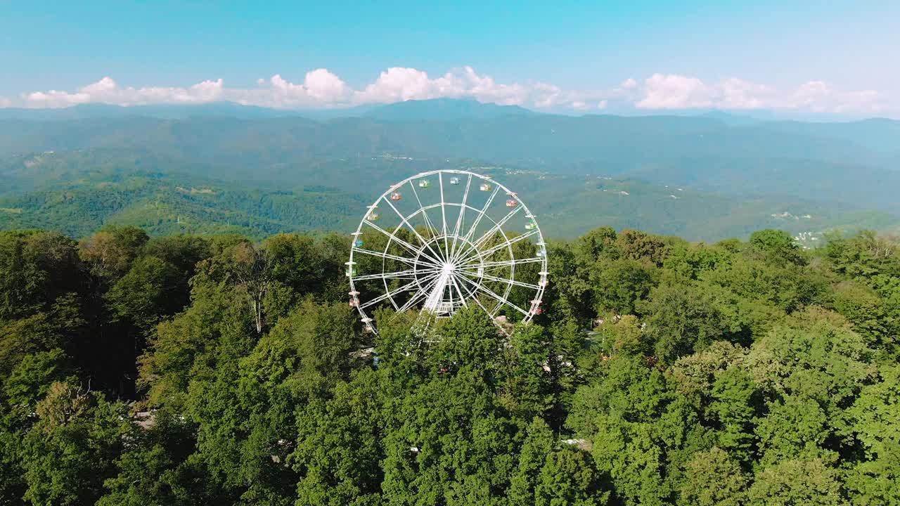 воздушный вид 4k. колесо обозрения вращается на вершине горы. потрясающий вид на горы и море. аттракцион для взрослых и детей