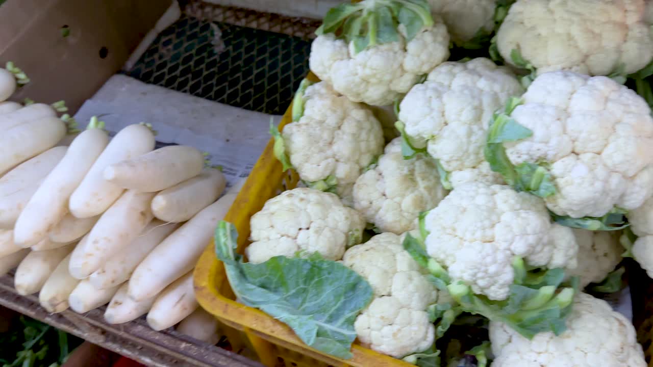 Hand selecting bananas, taro, cauliflower, and radish at vibrant outdoor Singapore vegetable market