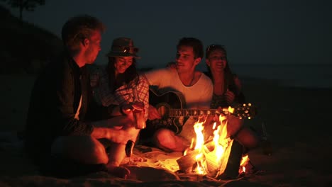 Picknick-Junger-Leute-Mit-Lagerfeuer-Am-Strand-Am-Abend.-Fröhliche-Freunde,-Die-Lieder-Singen-Und-Gitarre-Spielen.-Zeitlupe