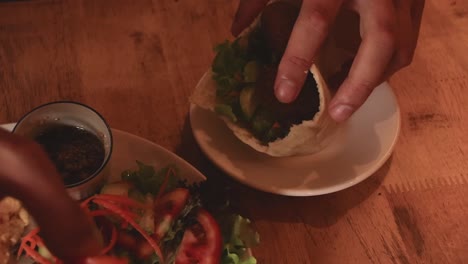 high angle view of hands stuffing falafel and fresh vegetable salad into a pita bread