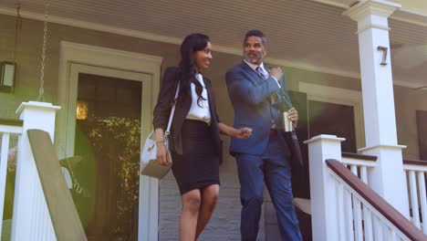 una pareja de negocios sale de una casa suburbana para ir a trabajar.