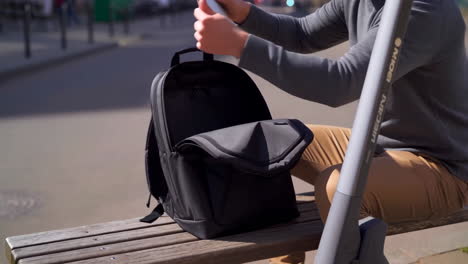man with backpack, laptop and scooter on a bench