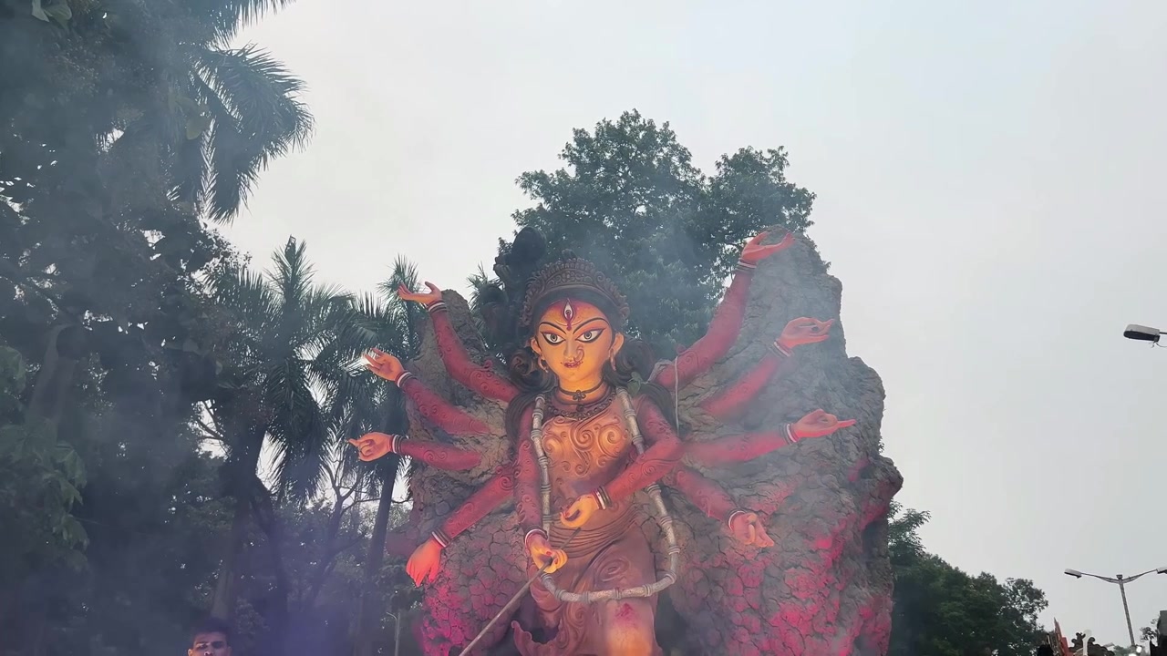 Uma tomada serena do ídolo de Maa Durga, com fumaça subindo suavemente em frente ao seu rosto e árvores ao fundo, ao anoitecer em Calcutá