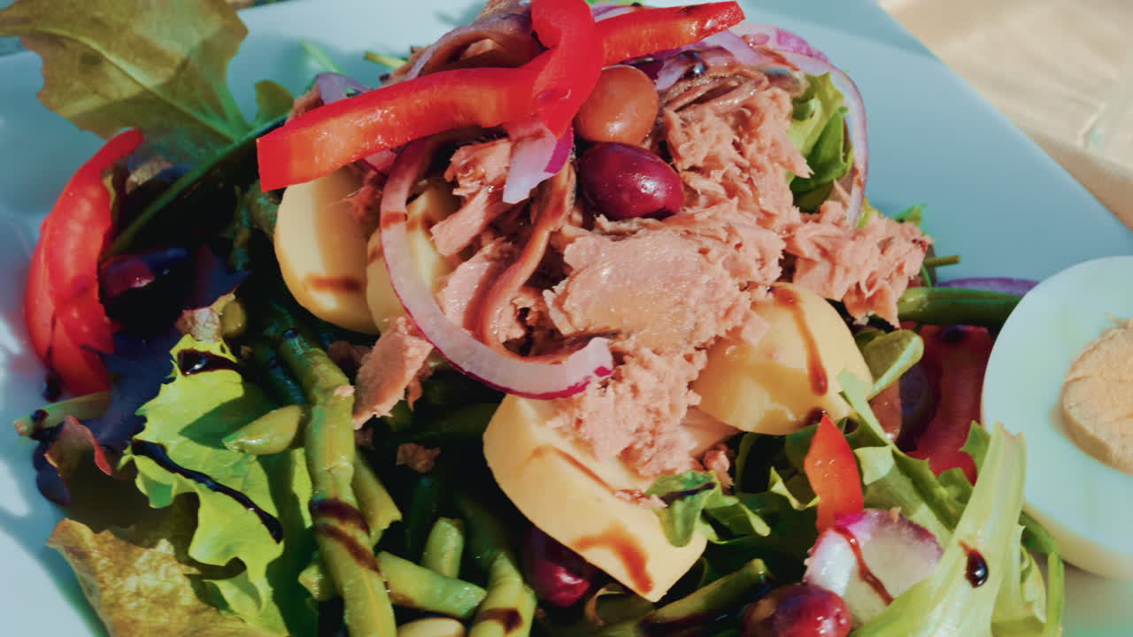 Close up of a colourful salad with tuna, potatoes, olives, red onion, peppers and mixed greens