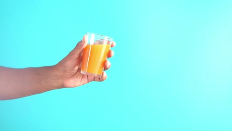 primer plano de una mano sosteniendo un vaso de jugo de naranja