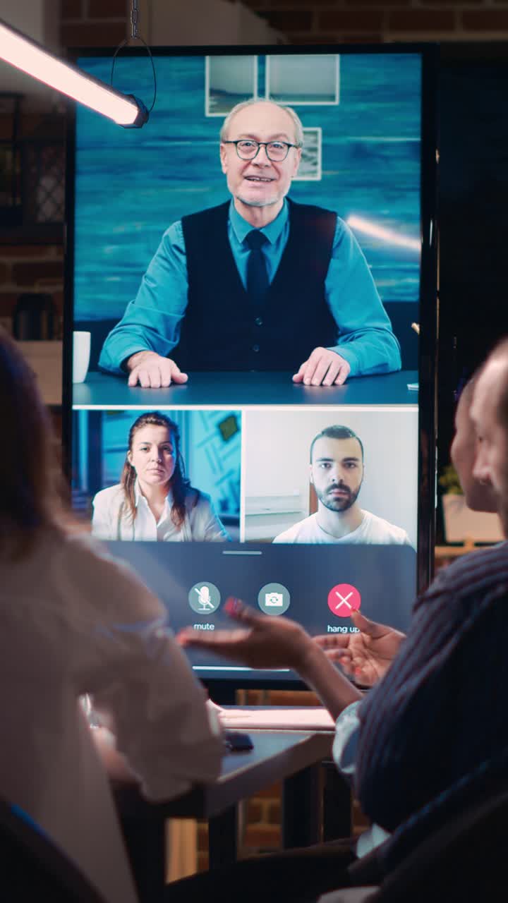 Vertical video: Employees greeting elderly executive in videocall, waving hi