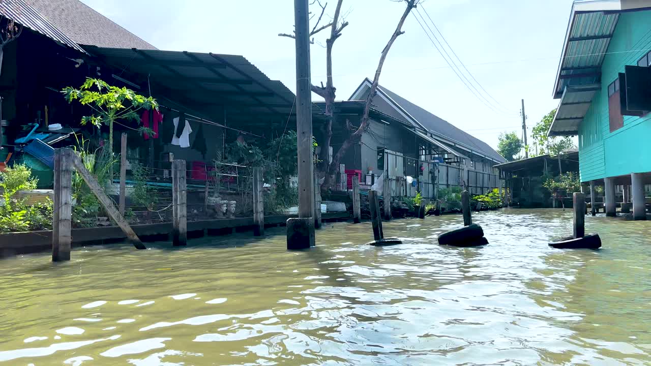 A serene boat ride along Bangkok's Khlong Lat Mayom Floating Market, showcasing vibrant stilt houses and lush greenery under bright daylight