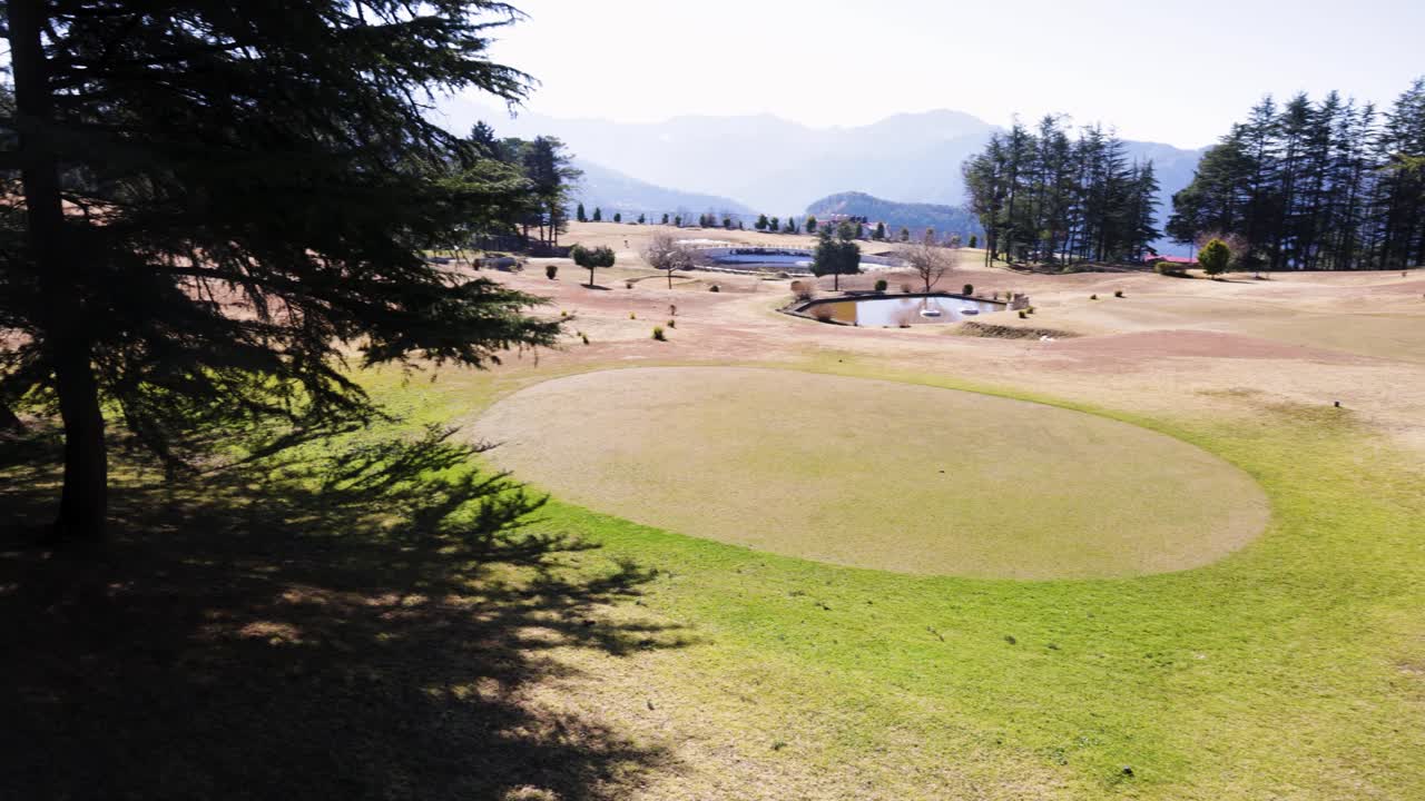 Campo da golf circondato da una pineta e catene montuose distanti.