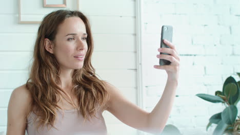 Retrato-De-Una-Mujer-Embarazada-Sonriente-Tomando-Una-Foto-Selfie-En-Un-Dormitorio-Luminoso.