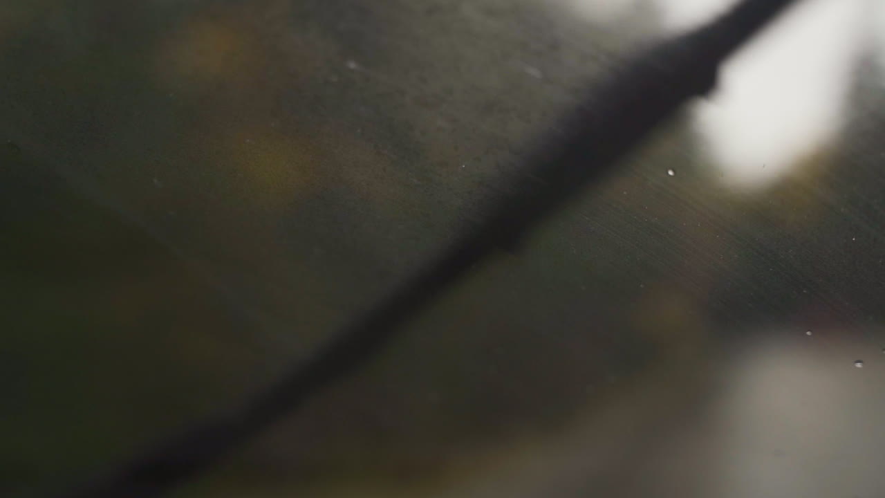Closeup wet rain hitting windshield and being cleaned by window wipers in slow motion