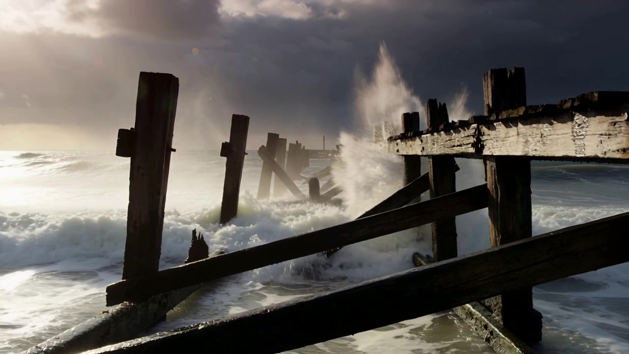 Onde tempestose che si infrangono su un molo di legno fatiscente sulla costa, dislocando un traverso