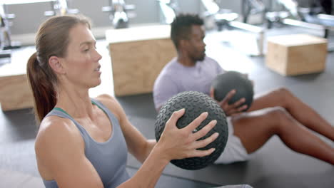 Fitte-Junge-Kaukasische-Frau-Und-Afroamerikanischer-Mann-Trainieren-Im-Fitnessstudio-Mit-Medizinbällen