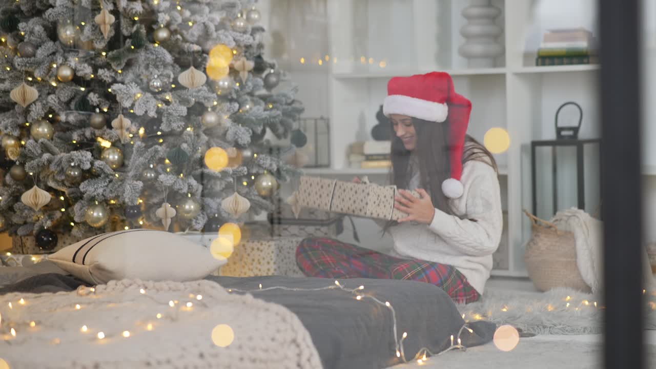mujer abriendo un regalo de navidad por el árbol de navidad