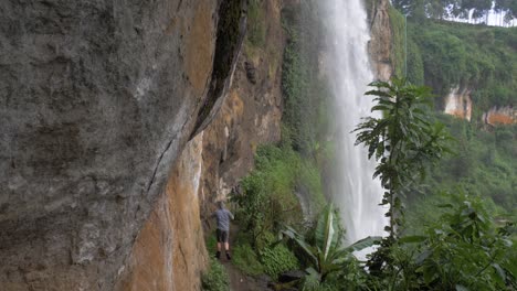 toma en cámara lenta de un excursionista caminando por un pequeño sendero de acantilado debajo de una cascada tropical