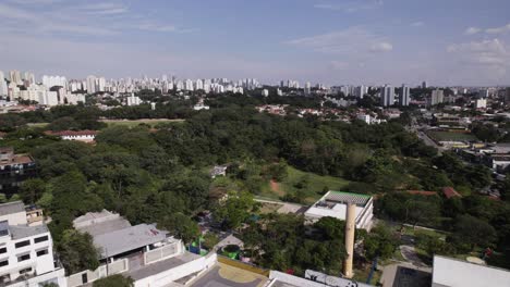 drone moves towards the city buildings passing by a grove with a little lake