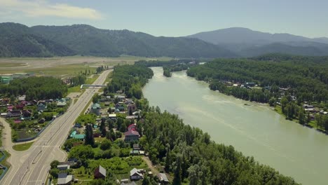 aerial flying over tourist town in the region of mountains mountain river and fields also view of the highway