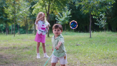 little children playing with soap bubbles in nature. pretty girl blowing colorful bubbles and small cute boy trying to catch them in the park.