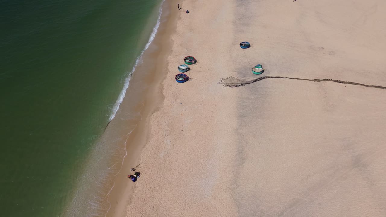 Drone performing a semi orbit above traditional round fishing boats on sandy Mui Ne beach, Vietnam.