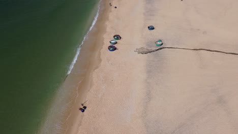 Drone performing a semi orbit above traditional round fishing boats on sandy Mui Ne beach, Vietnam.