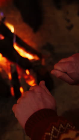 man warming hands by the fire indoors. cozy fireplace with burning wooden logs and flame warming male's hands . close-up. vertical video
