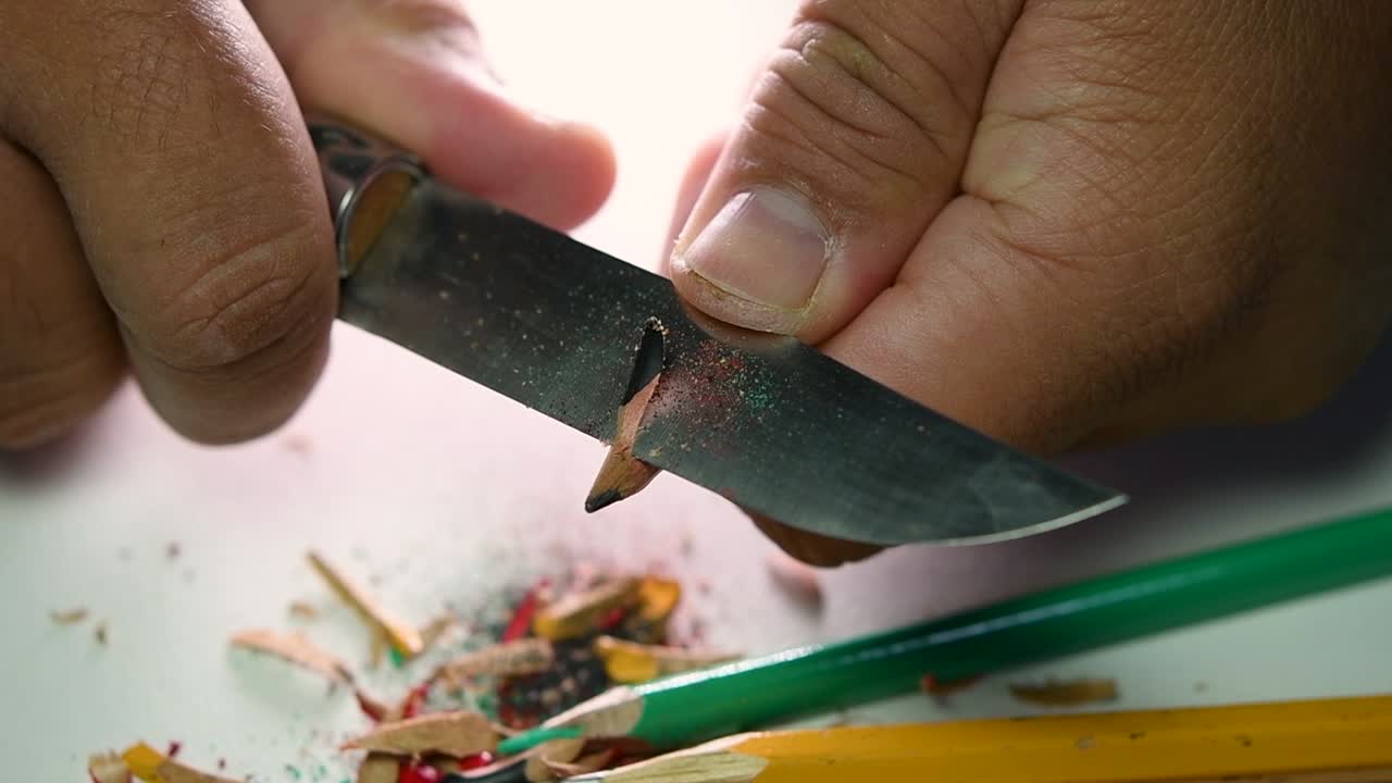Opptak av hender som sakte spisser en blyant og noen fargeblyanter med en skarp kniv