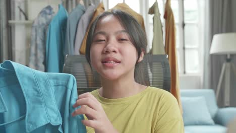 close up of asian young girl online seller recommending a shirt while using computer for selling clothes at home