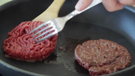 Flipping-two-rare-ground-beef-steaks-cooking-on-electric-modern-pan,-still-close-up-shot-indoors