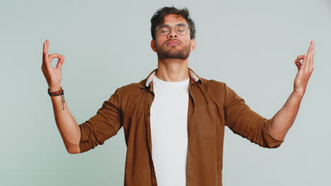 Indian-man-meditating-breathes-deeply-with-mudra-yoga-gesture,-eyes-closed,-taking-a-break,-relax