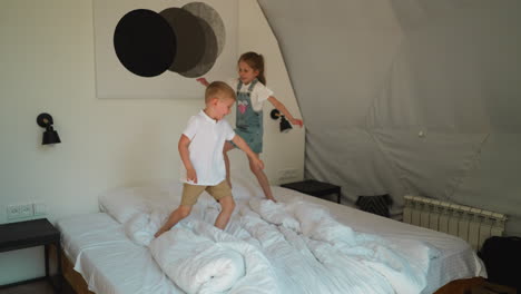 children run on large bed at glamping. joyful little brother and sister plays together in comfortable bedroom. happy healthy kids in hotel room