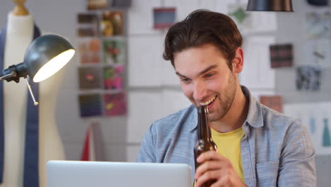 propietario masculino de un negocio de moda con una botella de cerveza haciendo una videollamada en una computadora portátil en el estudio