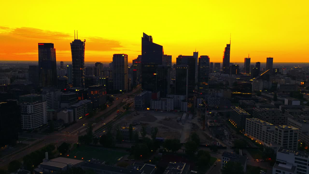 Wide aerial orbit view of Warsaw skyscrapers under glowing yellow sunrise