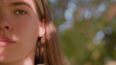 close-up of young lady looking intently with sunlight reflecting softly off her face, creating a serene yet focused expression, background is blurred with green hues