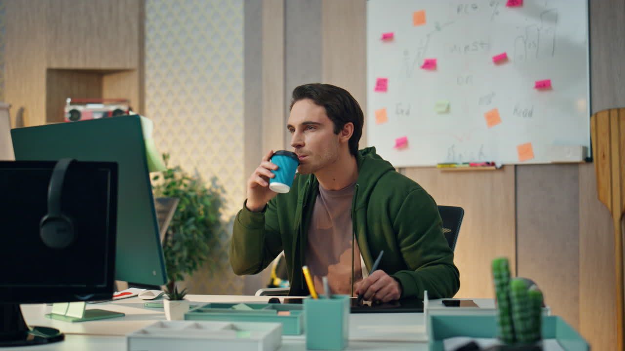 Designer rilassato che lavora al computer nell'home office. Uomo che beve tè e fissa il monitor.