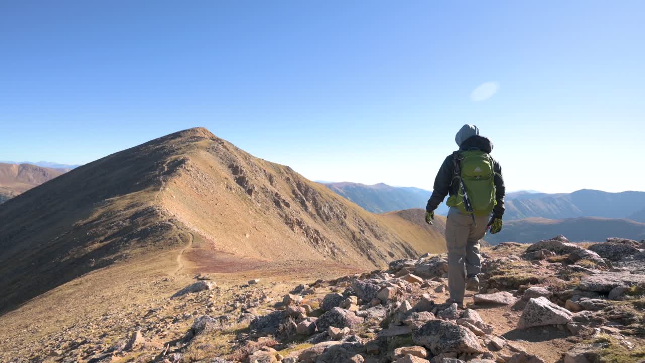 hombre caminando solo hacia una empinada subida de montaña en un día sin nubes, estático