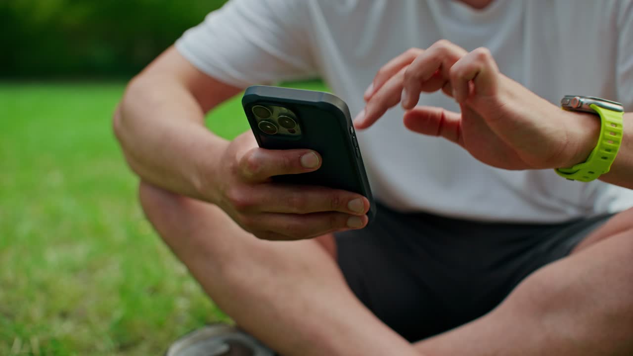 Persona che usa uno smartphone e uno smartwatch su un prato