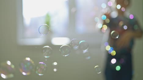 round colorful bubbles flying in the room on the blurred background with a boy. beautiful soap bubbles and a silhouette of a boy playing with them indoors.
