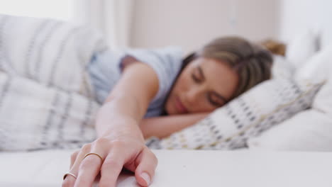 Woman-Asleep-In-Bed-Reaches-Out-To-Turn-Off-Alarm-Clock-On-Bedside-Table