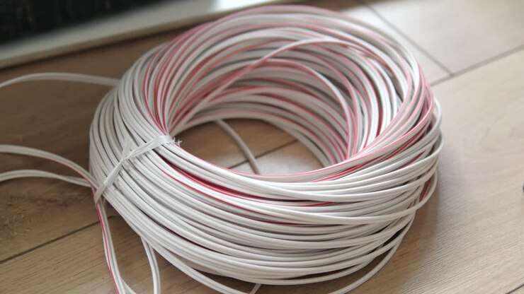 Close-up of a coil of white electrical wire with a red stripe, on a wooden floor