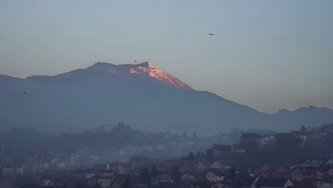 Crows-fly-in-city-at-twilight-with-big-mountain-in-the-background