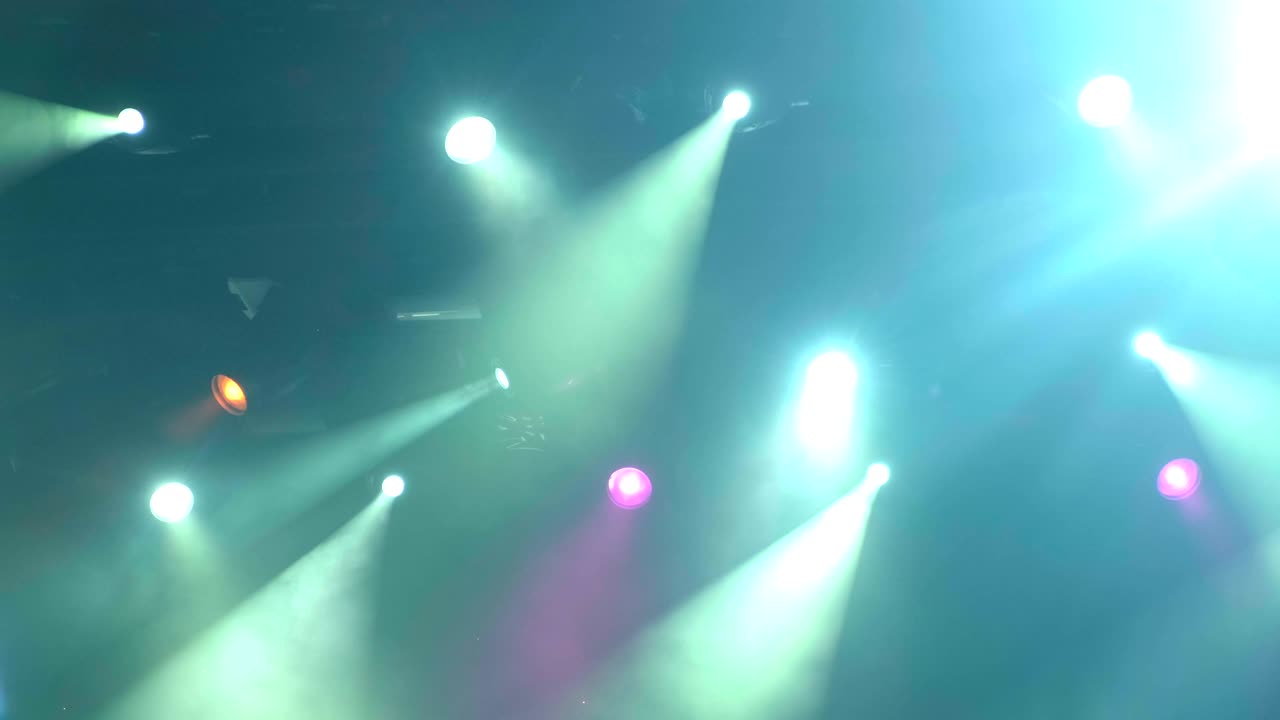 4k uhd handheld Lighting equipment on the stage of the concert during the performance. The light rays from the spotlight through the smoke. Blue and yellow  purple green rays of light
